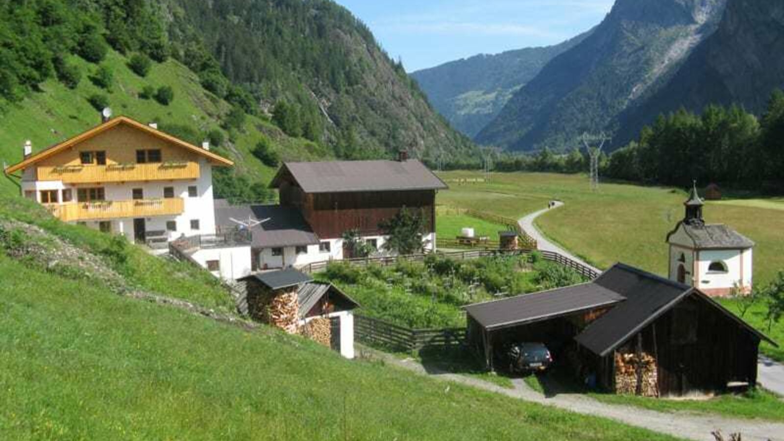 Vista da sud (vista panoramica sull'intera fattoria): Sala di affumicatura, sala caldaia con garage, cappella privata con abitazione e fabbricato agricolo; vista sul prato e sulla valle di Umhausen - sullo sfondo le piste da sci e gli itinerari per escursioni di Hochötz